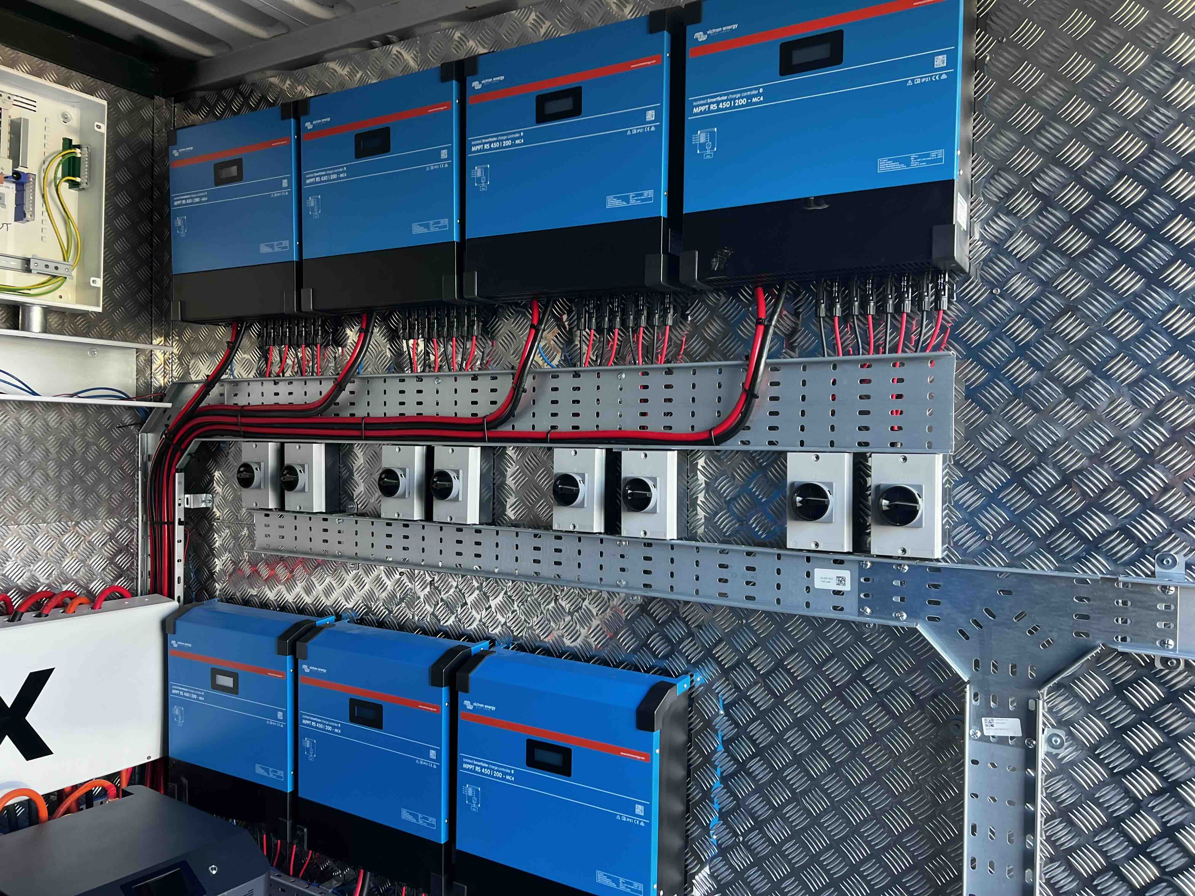 Seven Victron MPPT charge controllers wired on the wall of a WattBox container